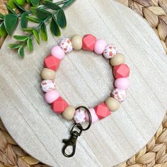 a pink and beige beaded bracelet sitting on top of a wooden table next to a plant