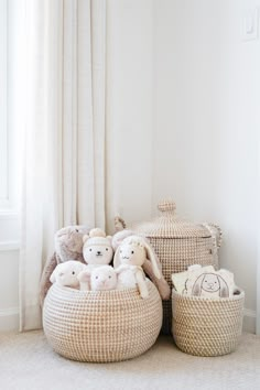 several stuffed animals are sitting in baskets on the floor next to a curtained window