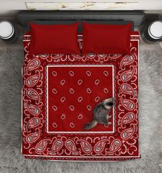 a cat sitting on top of a red bandana bedding set with two pillows