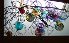 there are many glass balls hanging from the tree branch in front of the window sill