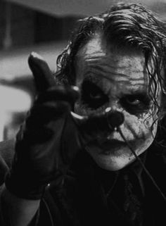 the joker is holding his hands up in front of his face and pointing at something