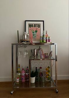 a bar cart filled with bottles and glasses on top of a hard wood floor next to a wall