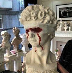 a man standing next to a white statue with blood on it's face and head