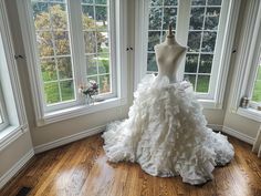 a mannequin dressed in a white wedding dress sits on a wooden floor next to three windows