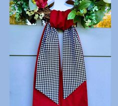 a red and black tie hanging on the side of a wall next to some flowers