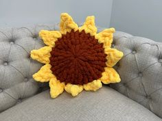 a crocheted sunflower sitting on top of a gray couch next to a wall