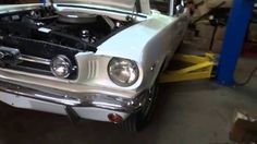 an old white mustang car with its hood up in a garage, it is being worked on