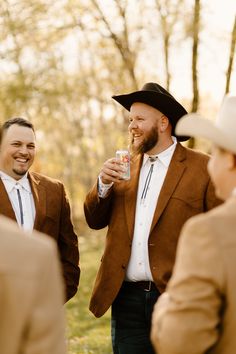 two men in brown jackets and hats are having drinks while another man is wearing a cowboy hat