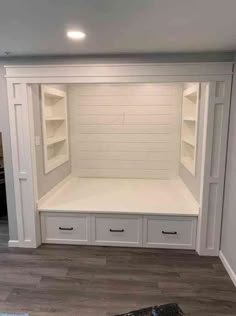 an empty room with white shelves and drawers on the wall, in front of a wooden floor