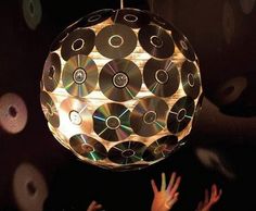 a person reaching up to a disco ball with cds on it and hands in the air