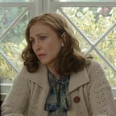 a woman sitting at a table in front of a window looking off into the distance