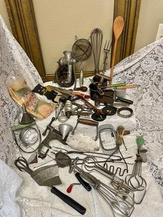 an assortment of kitchen utensils on a white lace tablecloth in front of a gold framed mirror