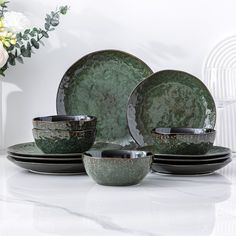 a set of green and black dinnerware with flowers in the background