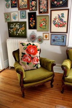 two green chairs sitting next to each other on top of a hard wood floor covered in framed pictures