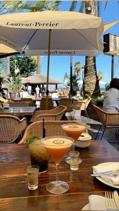 two cocktails sitting on top of a wooden table next to an umbrella over it