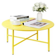 a yellow coffee table with flowers and books on it, sitting next to a white vase