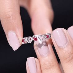 a woman's hand holding a ring with two hearts and garnets on it