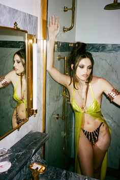 a woman in a yellow bathing suit standing in front of a mirror with her arms up