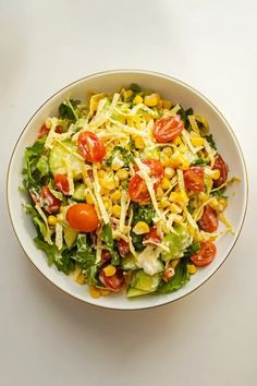 a white bowl filled with salad topped with corn and tomatoes on top of a table