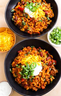 two black bowls filled with chili macaroni and cheese on top of a table