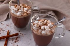 two mugs filled with hot chocolate and marshmallows on top of a table