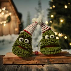 two green crocheted christmas mittens with googly eyes sitting on top of a wooden board