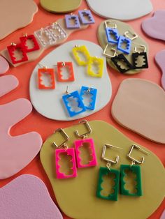 several pairs of colorful earrings sitting on top of a pink and yellow table with different shapes