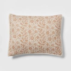 an orange and white floral pillow on a white surface with a light brown border around it