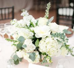 a vase filled with white flowers and greenery on top of a dining room table