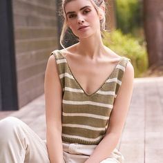 a young woman sitting on the ground wearing white pants and a striped top, with her hands in her pockets