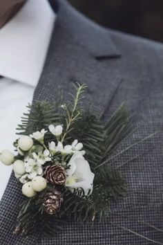 a boutonniere with white flowers and pine cones is worn by a man in a suit