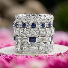 a stack of wedding rings with blue and white stones on top of each other in front of pink flowers