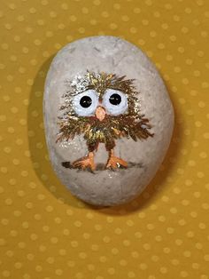 a painted rock with an owl on it's face and gold glitters around its eyes