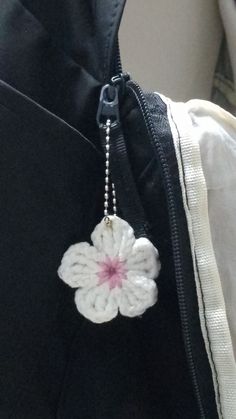 a white crocheted flower is hanging from a black zippered bag with a chain