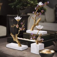 three white and gold vases with flowers in them sitting on a table next to a potted plant