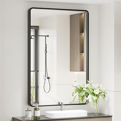 a bathroom sink sitting under a mirror next to a vase with flowers on top of it