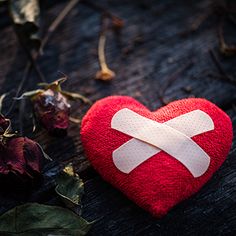 a red heart with a white cross on it sitting next to some dead flowers and leaves