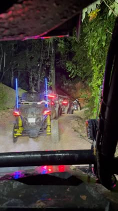 some cars driving down a dirt road with lights on at the top and behind them