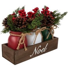 two vases filled with pine cones and red berries on top of a wooden box