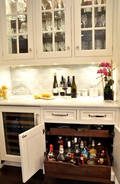 an open refrigerator in a kitchen with bottles and glasses