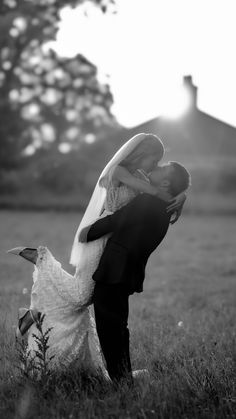 a bride and groom kissing in the middle of a field at their wedding day, with the sun shining behind them