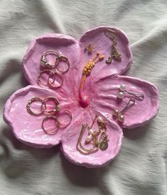 a pink flower with lots of rings and jewelry on it's center, sitting on a white sheet