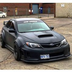 a black subarunt parked in front of a brick building with one word written on it