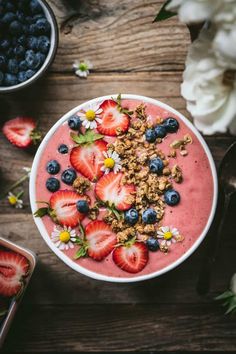 a bowl filled with fruit and granola on top of a wooden table next to flowers