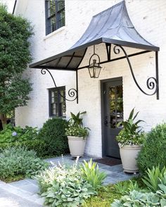 a white brick house with two large planters on the front porch and an awning over the door