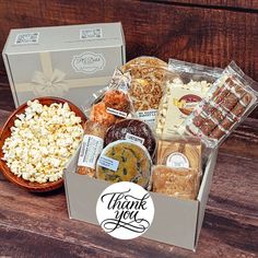 a thank you gift box filled with popcorn, cookies and other treats on a wooden table