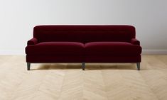 a red couch sitting on top of a hard wood floor next to a white wall