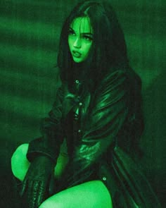 a woman with green makeup and black leather outfit sitting on a stool in the dark