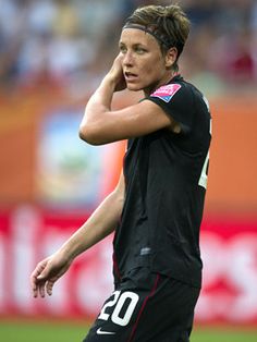 a female soccer player is on the field with her hand to her ear and looking down