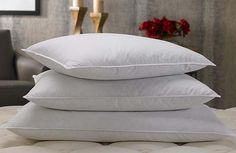 three white pillows stacked on top of each other in front of a chair and vase